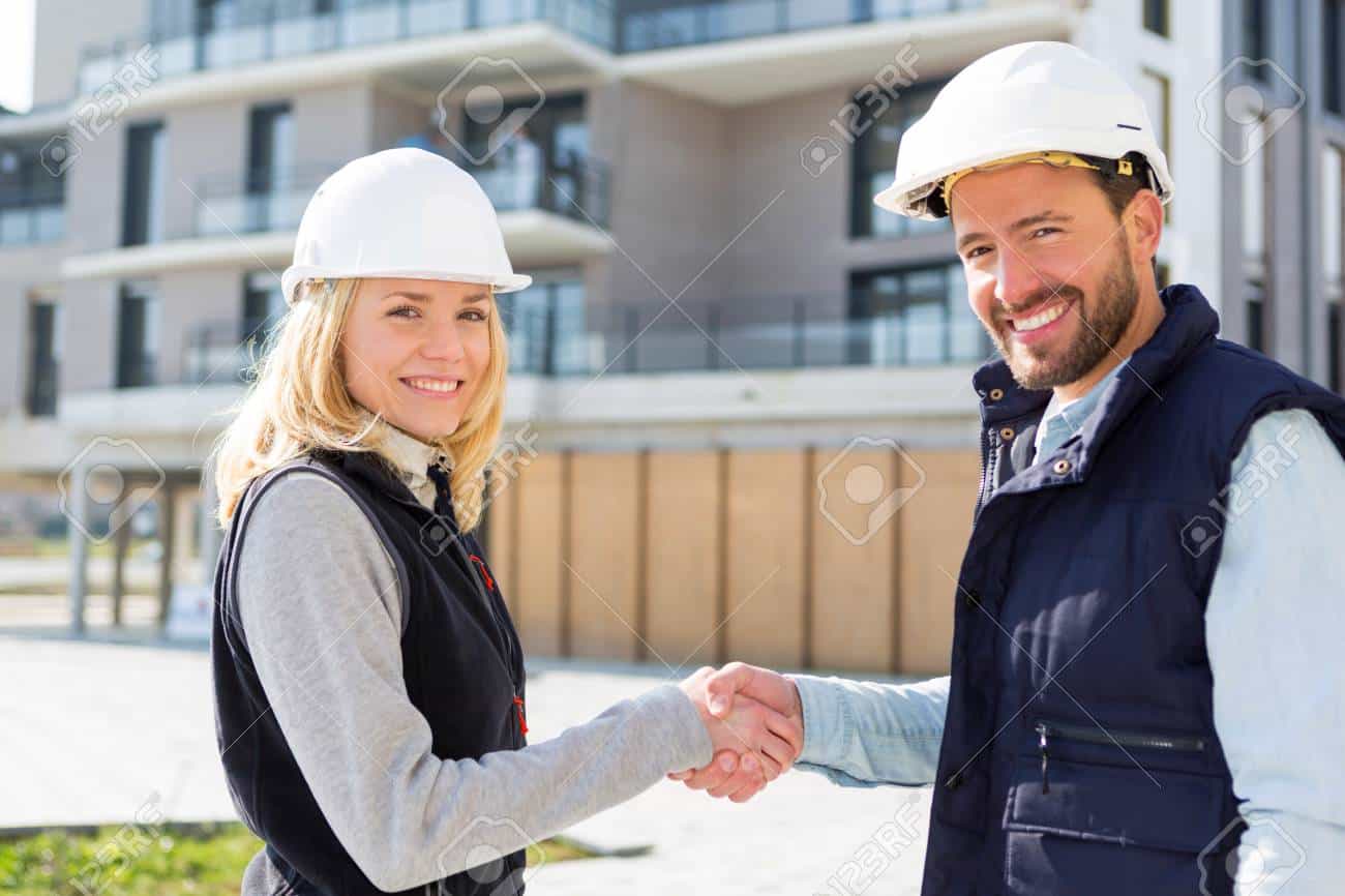 An architect and a construction worker shaking hands on a building site.