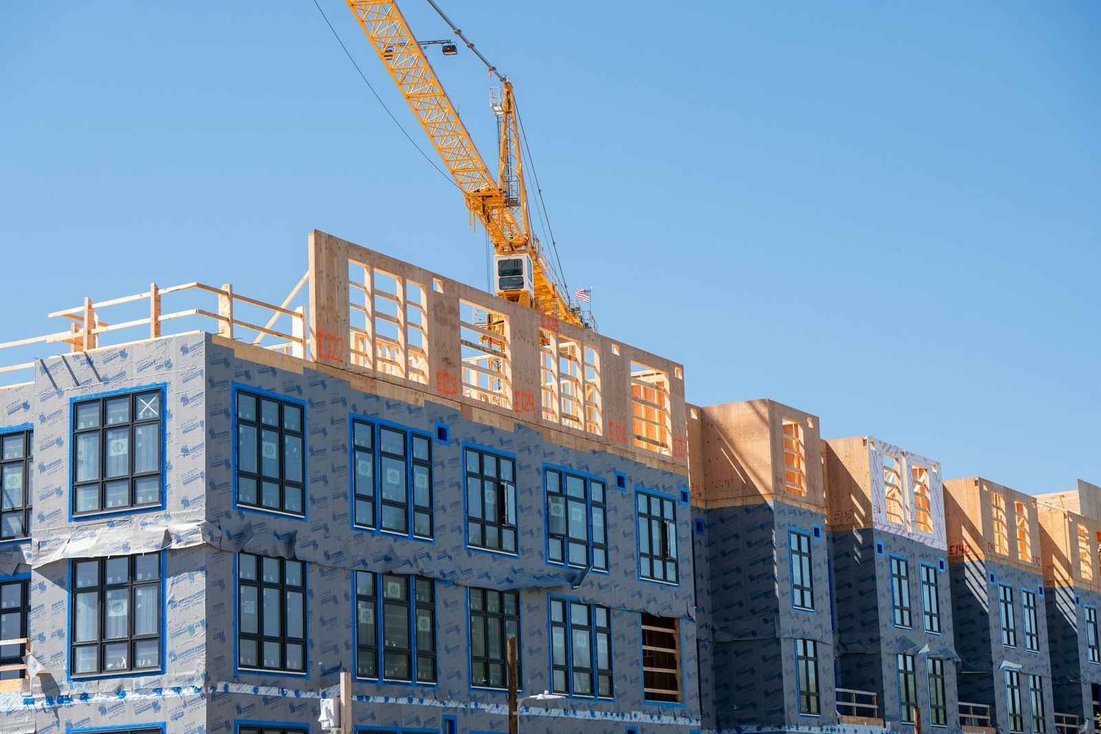 A multi-family apartment building under construction, with a tower crane above the framed upper floors.